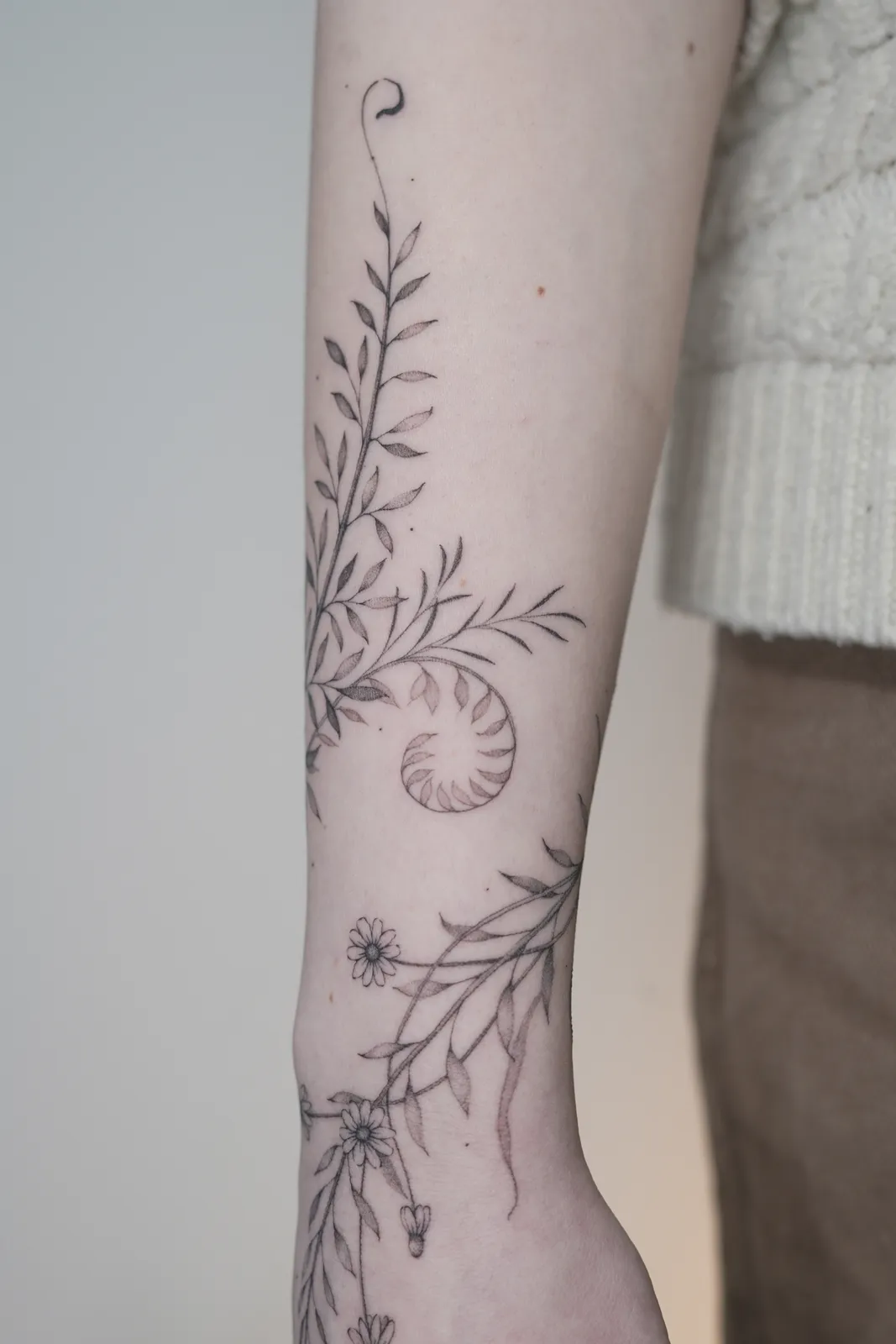 Detalhe de tatuagem fineline: ramos ornamentais no antebra&ccedil;o