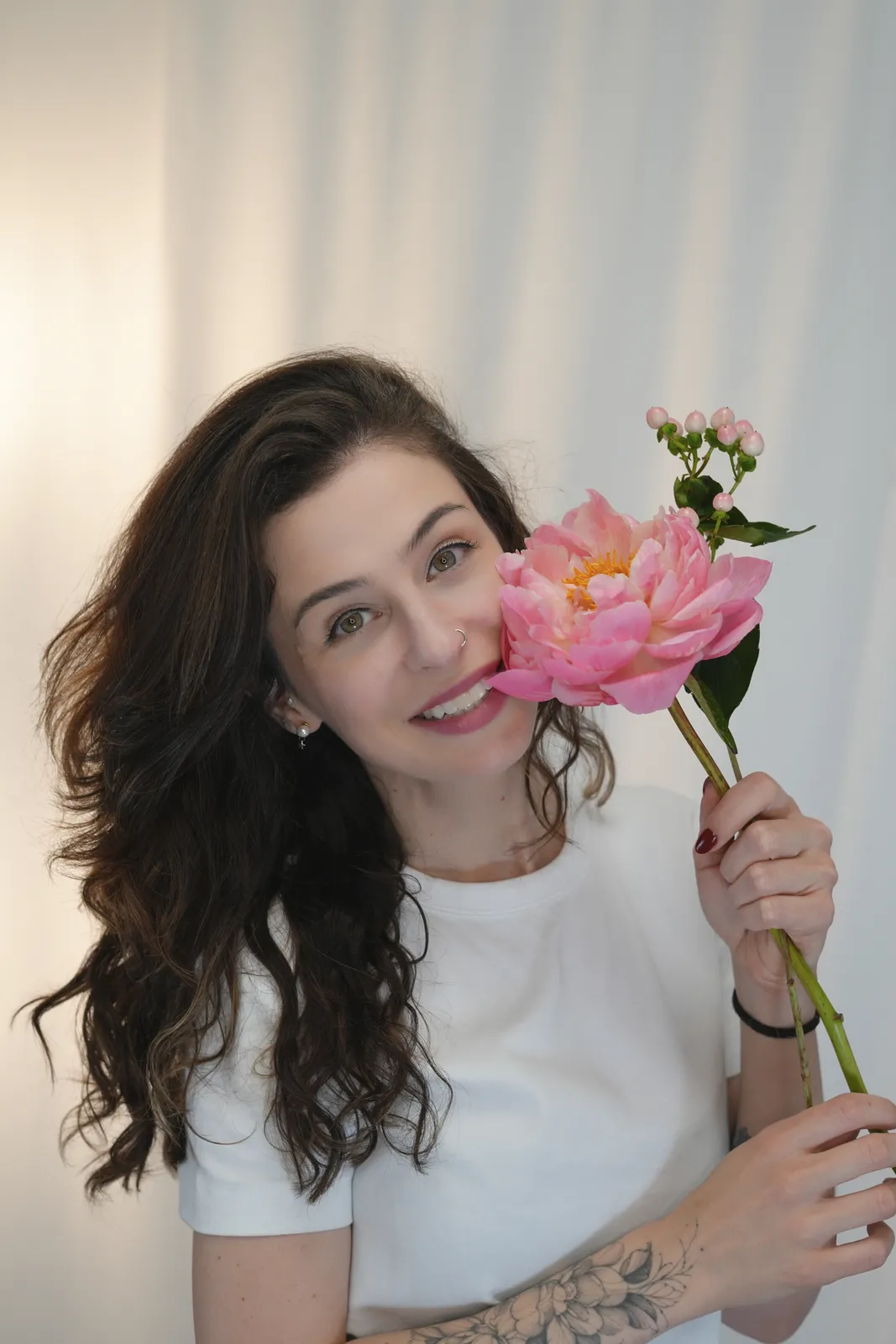 Talita segurando uma pe&ocirc;nia rosa junto ao rosto, sorrindo