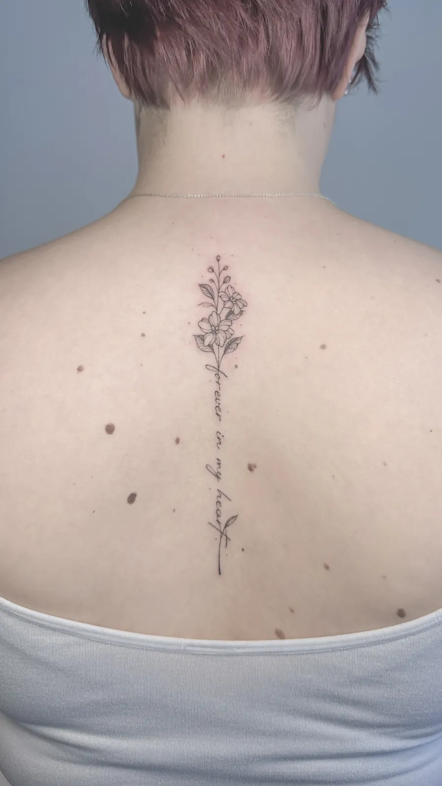 Tatuagem floral com a frase forever in my heart na coluna